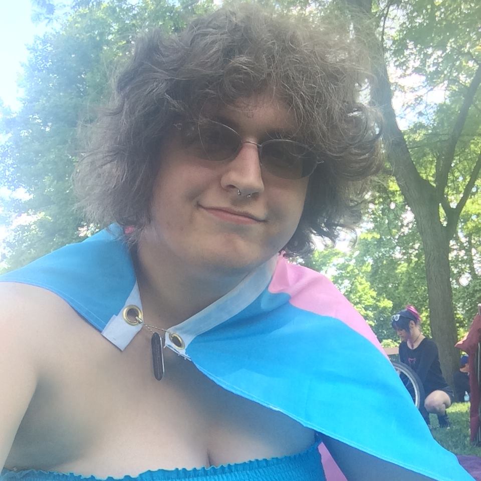 Jennifer at a pride event, wearing a trans flag as a cape